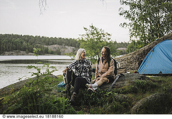 Smiling senior women talking to each other while sitting on rock during camping