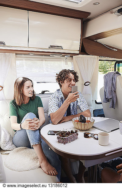 Smiling siblings relaxing at table in motor home during summer vacation