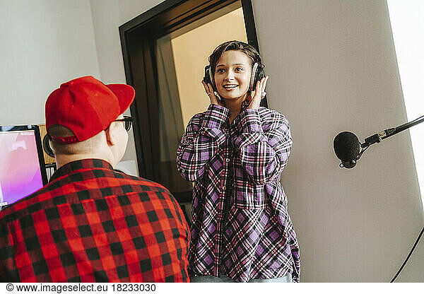 Smiling singer wearing headphones singing in front of colleague at studio