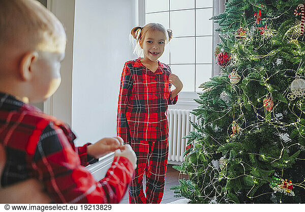 Smiling sister looking at brother near Christmas tree at home