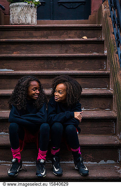 Smiling sisters in sports clothing sitting on steps