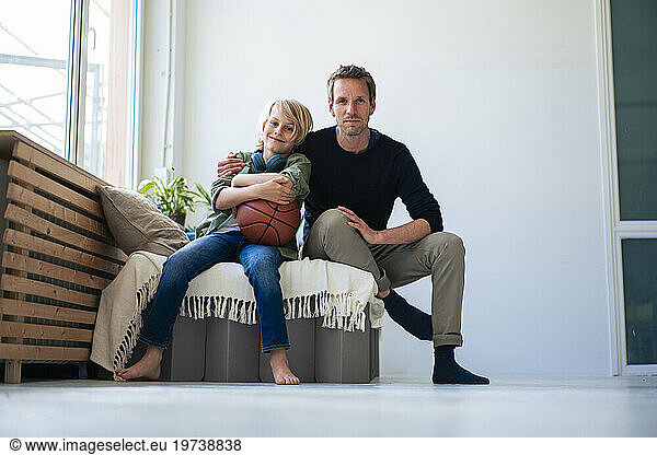 Smiling son holding basketball and sitting with father at home