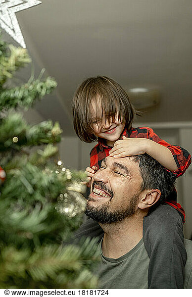 Smiling son playing with father by Christmas tree at home