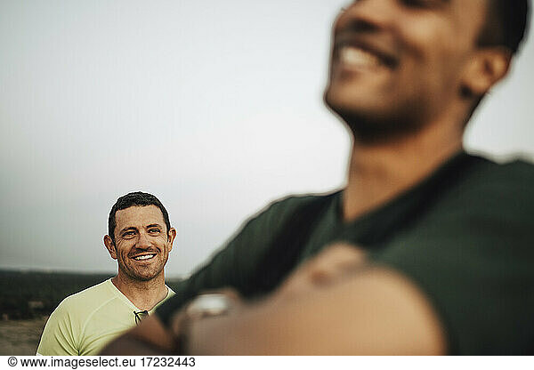Smiling sportsman looking at male athlete against sky during sunset