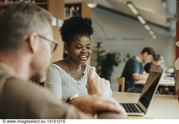 Smiling student discussing with professor over laptop in library at university