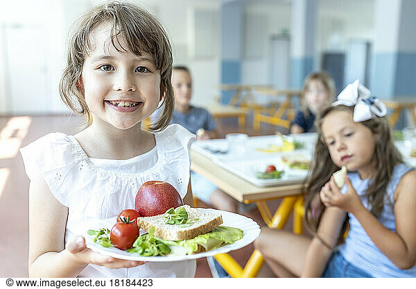 Smiling student holding healthy meal on plate standing at cafeteria