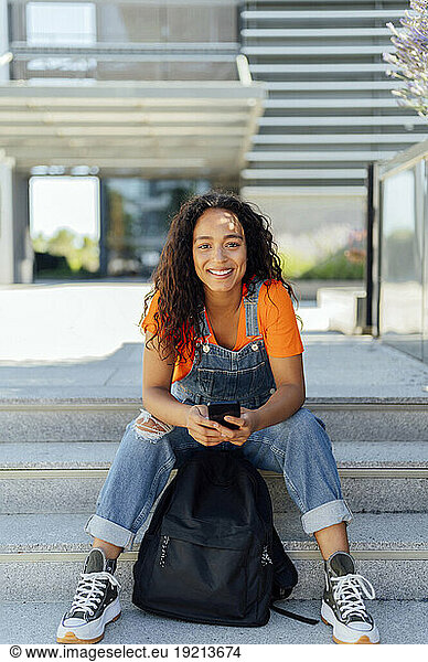Smiling student with backpack sitting on steps in campus