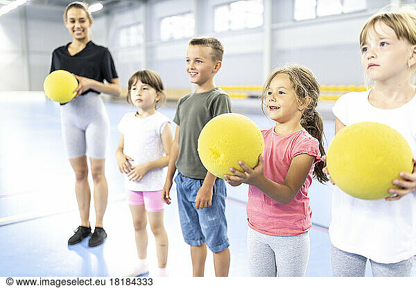 Smiling students holding ball with teacher standing at school sports court