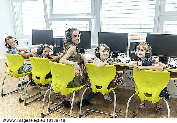 Smiling students with teacher wearing headphones sitting in computer class at school