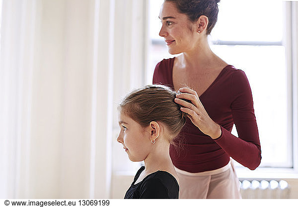 Smiling teacher adjusting ballerina's hair bun in studio