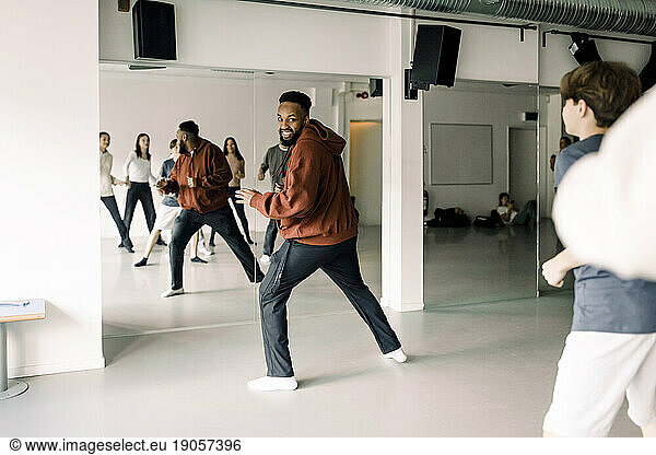 Smiling teacher looking at teenage students practicing dance in studio at high school