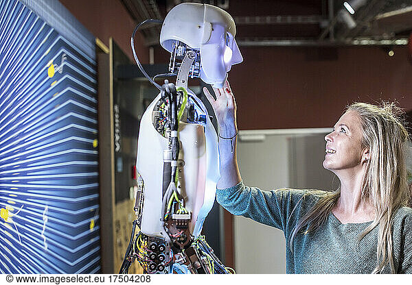 Smiling tech developer touching human robot face at workshop