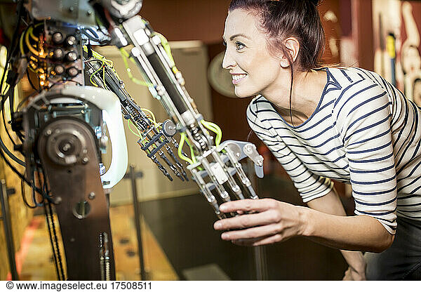 Smiling technician shaking hand with human robot at workshop