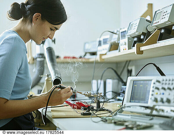 Smiling technician with work tool soldering electronic equipment at desk in laboratory