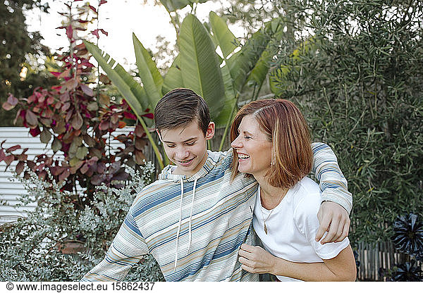 Smiling teen boy hugging laughing mom in front of lush plants