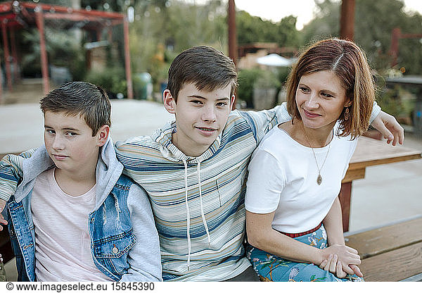 Smiling teen boy with arms around brother and youthful mid-40's mom