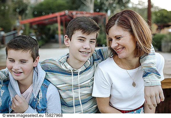Smiling teen boy with braces hugs mom and younger brother