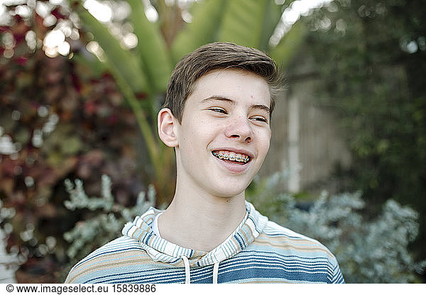 Smiling teen boy with braces in front of tropical plants