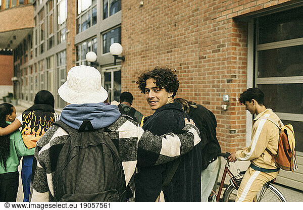 Smiling teenage boy looking over shoulder while walking with friends on sidewalk