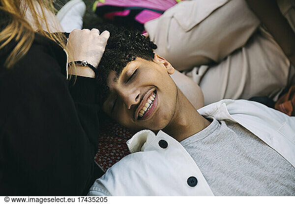Smiling teenage boy lying with head on lap of female friend