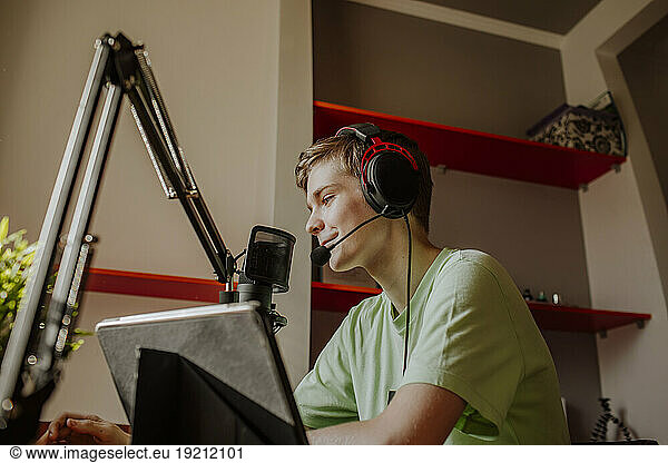 Smiling teenage boy podcasting near laptop at home