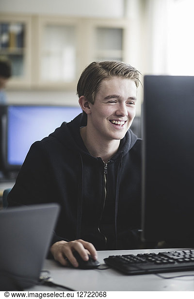 Smiling teenage boy using computer in classroom at high school