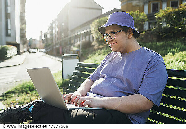 Smiling teenage boy using laptop on bench in park