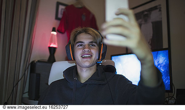 Smiling teenage boy with headphones taking selfie with smart phone