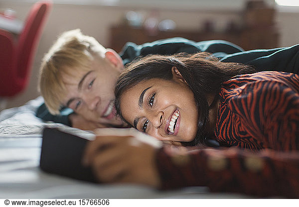 Smiling teenage couple using smart phone on bed