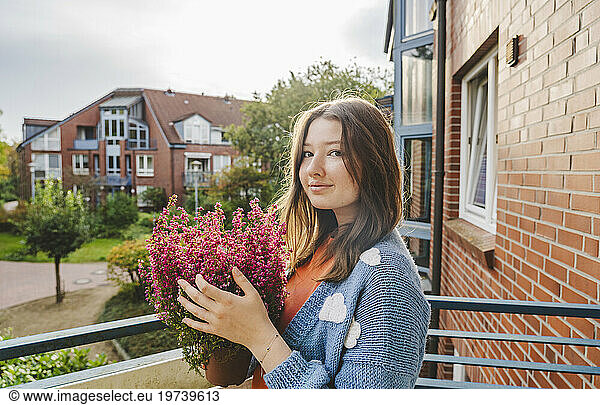 Smiling teenage girl holding heather flowering plant in balcony