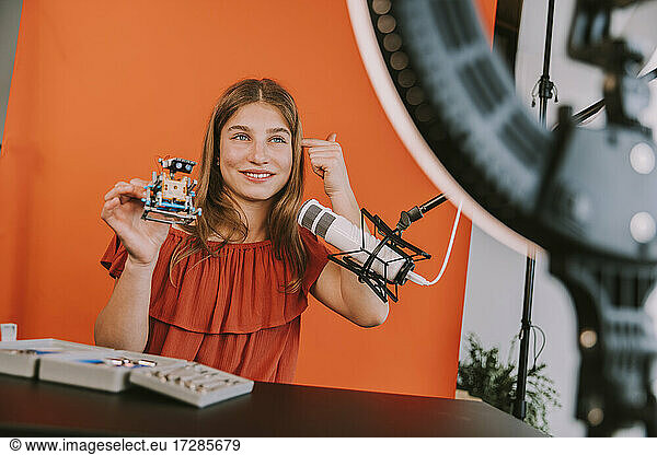 Smiling teenage girl holding robot model while vlogging at home