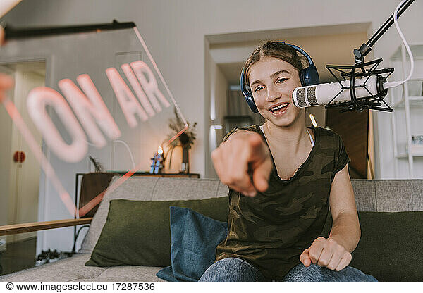 Smiling teenage girl pointing while broadcasting at home