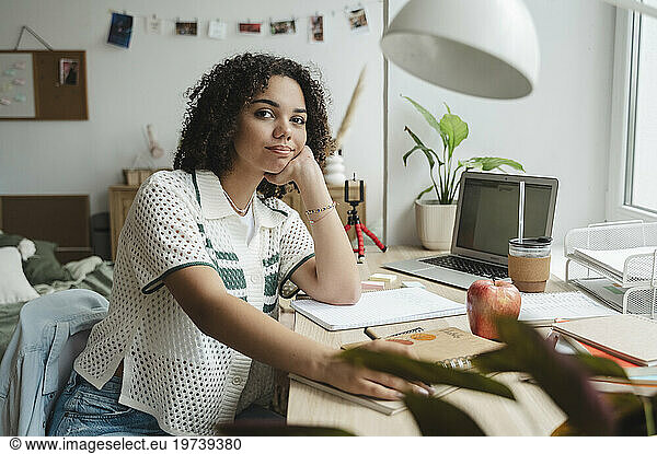Smiling teenage girl sitting at desk in bedroom
