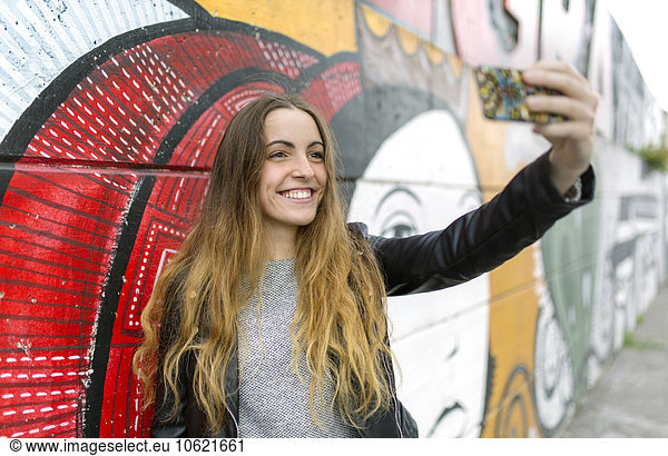 Smiling teenage girl taking a selfie at mural