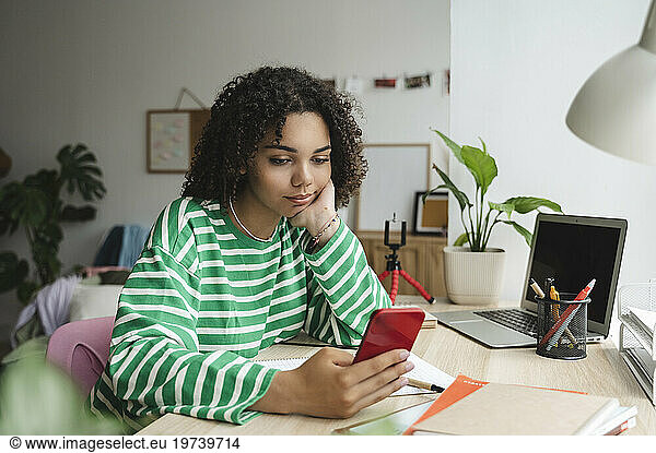 Smiling teenage girl using smart phone at desk in bedroom