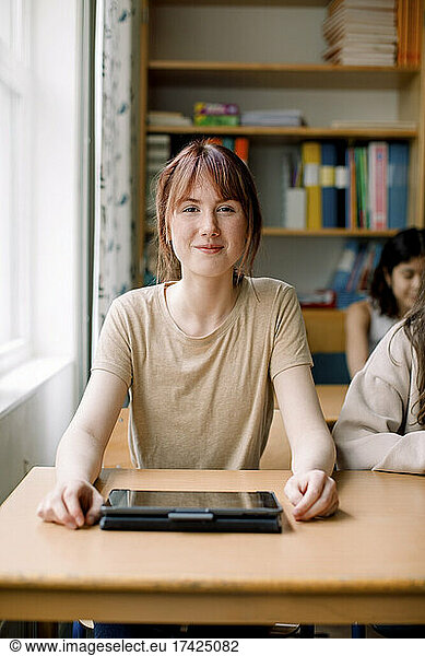 Smiling teenage girl with digital tablet on desk in classroom