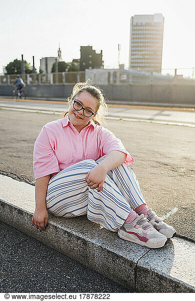 Smiling teenage girl with down syndrome sitting on footpath