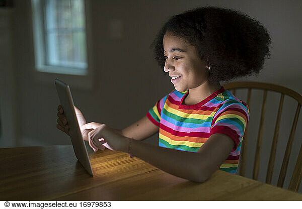 Smiling ten year-old bi-racial girl working on ipad at table