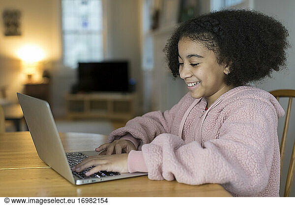 Smiling ten year-old bi-racial girl working on laptop at table