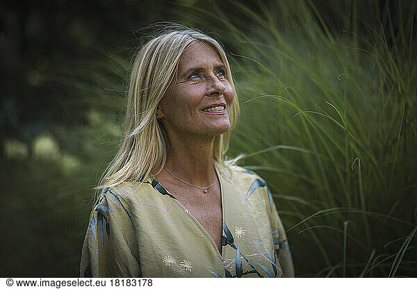 Smiling thoughtful mature woman in blond hair at garden