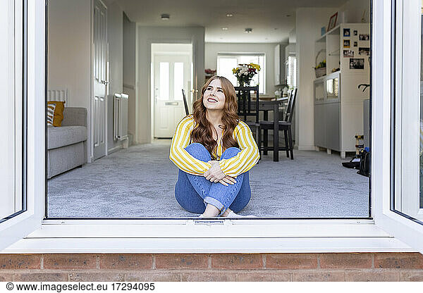 Smiling thoughtful redhead woman sitting by window looking away