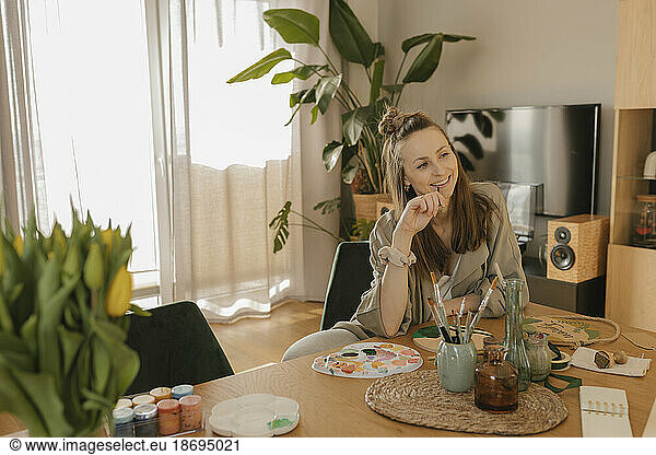 Smiling thoughtful young woman painting while sitting at table