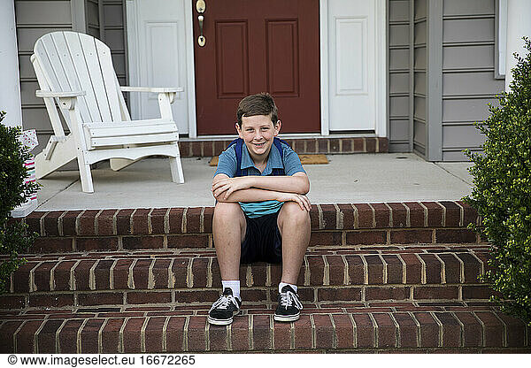 Smiling Tween Boy With Braces Sits on Brick Front Steps