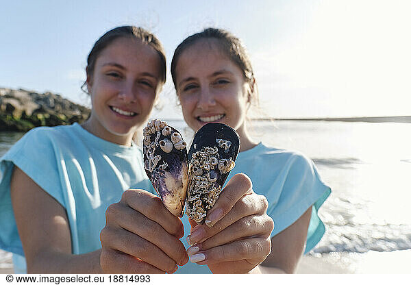 Smiling twin sisters holding seashells at beach