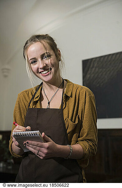 Smiling waitress in apron taking order at restaurant