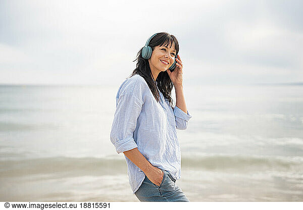 Smiling woman adjusting bluetooth headphones at beach