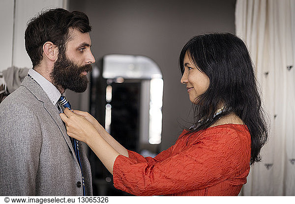 Smiling woman adjusting necktie on husband at home