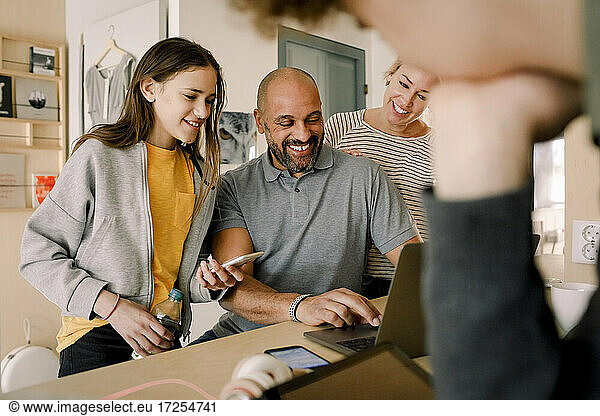 Smiling woman and daughter looking at man doing online shopping at home