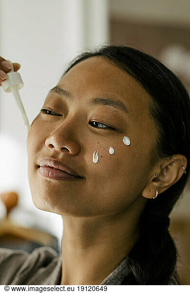 Smiling woman applying cream on face