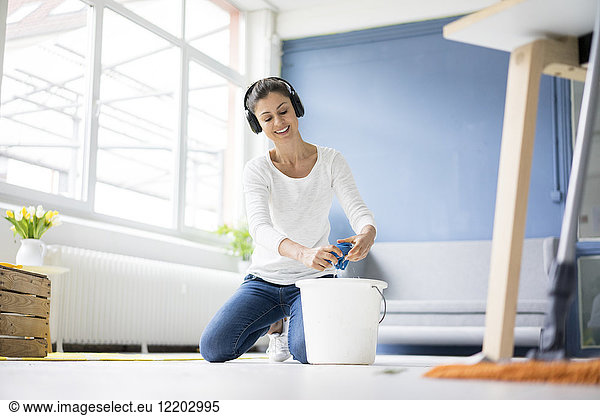 Smiling woman at home wearing headphones wiping the floor